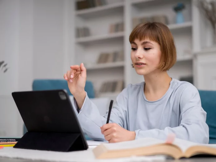 Female student using tablet and notes to stay focused during online classes at home.