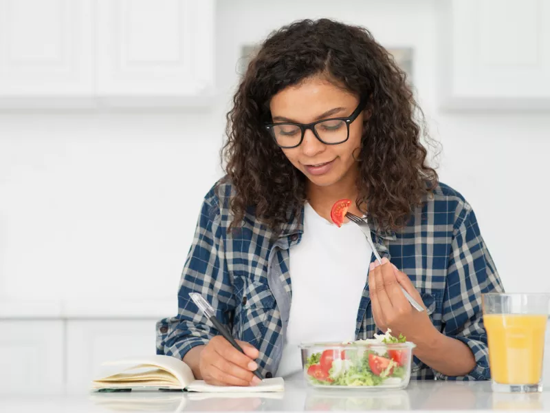 Student journaling while eating a healthy lunch to Stay Productive During Midterms and study sessions.